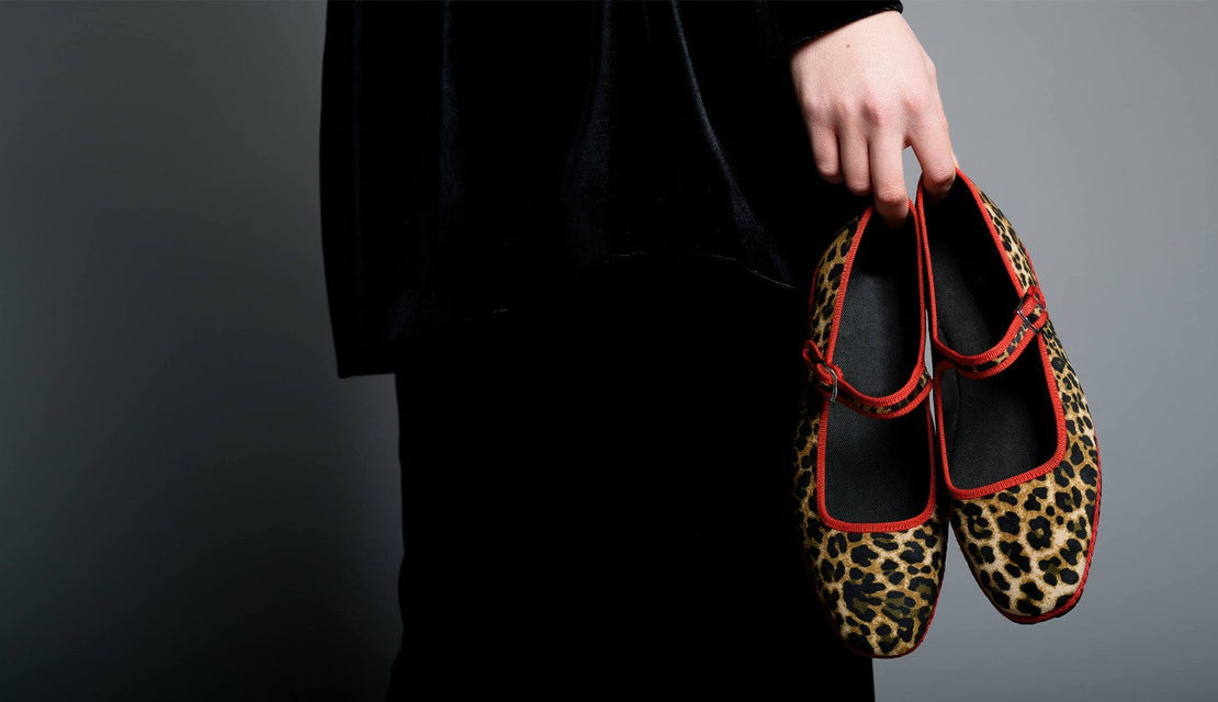 Person holding a pair of leopard print shoes with red accents against a dark background